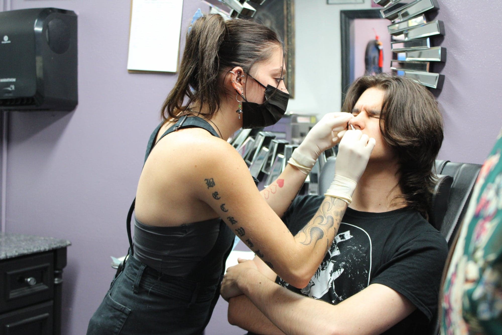 A piercer performing a nose piercing on a client