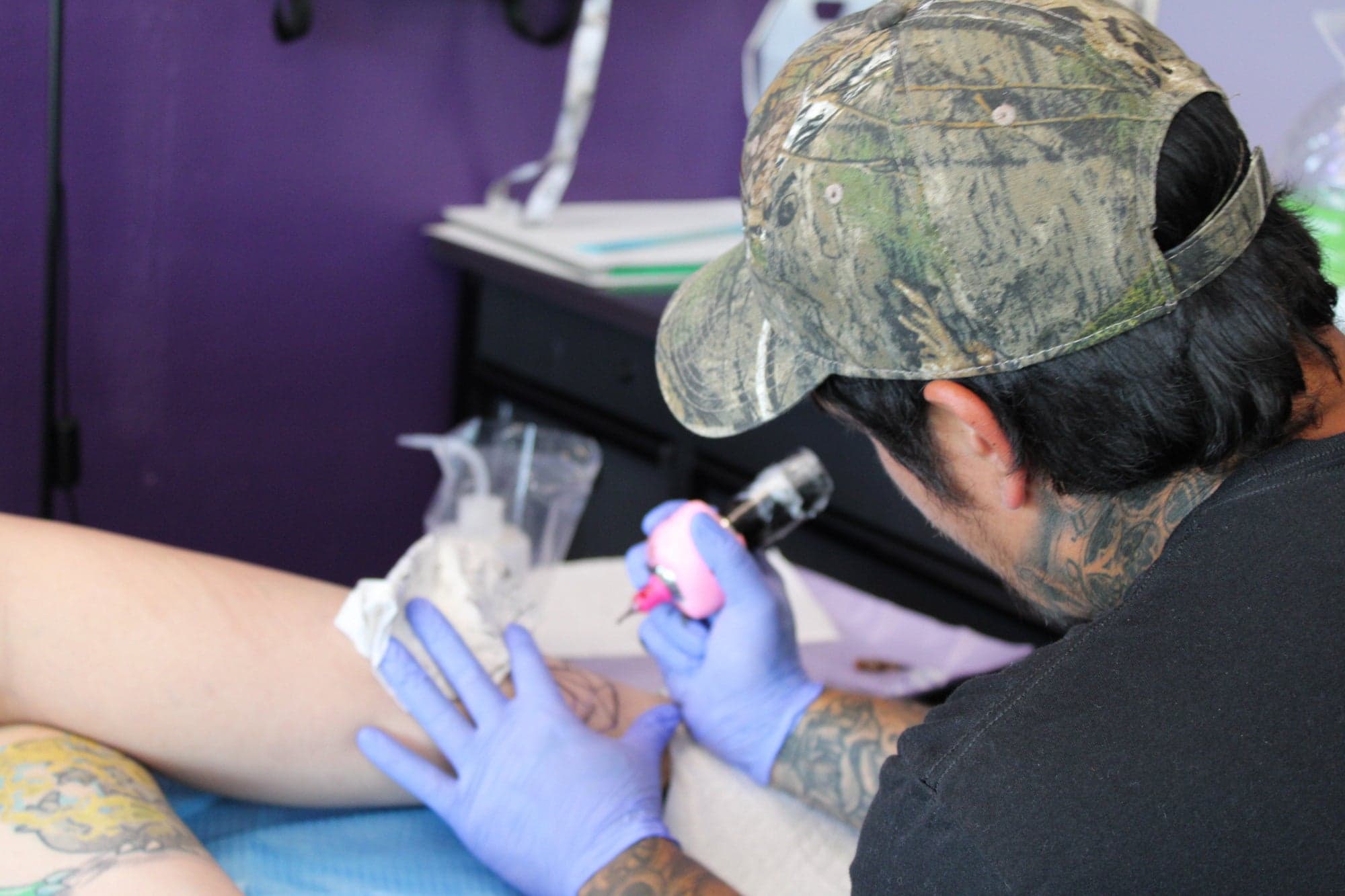 A tattoo artist working linework on a client's forearm